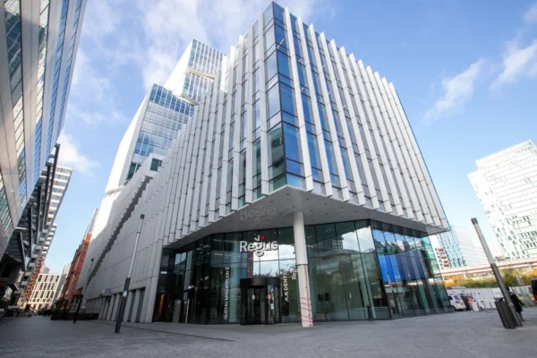 Een modern kantoorgebouw met veel glas en geometrische lijnen onder een blauwe lucht.