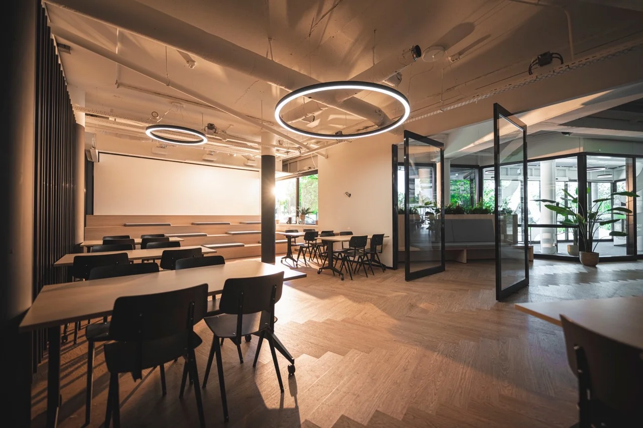 Moderne, open vergaderruimte met houten vloer, tribunezitplaatsen en ronde plafondverlichting.