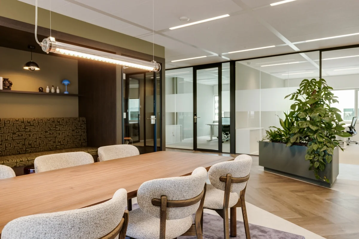 Moderne kantoorruimte met glazen wanden, een houten tafel met stoelen, en een grote groene plant.
