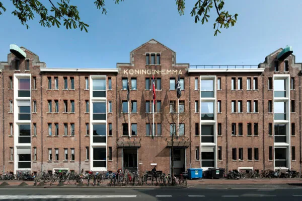 Voorgevel van het HNK-gebouw in de Amsterdamse Houthavens, met de naam "Koningin Emma" op de gevel en fietsen geparkeerd voor de ingang.