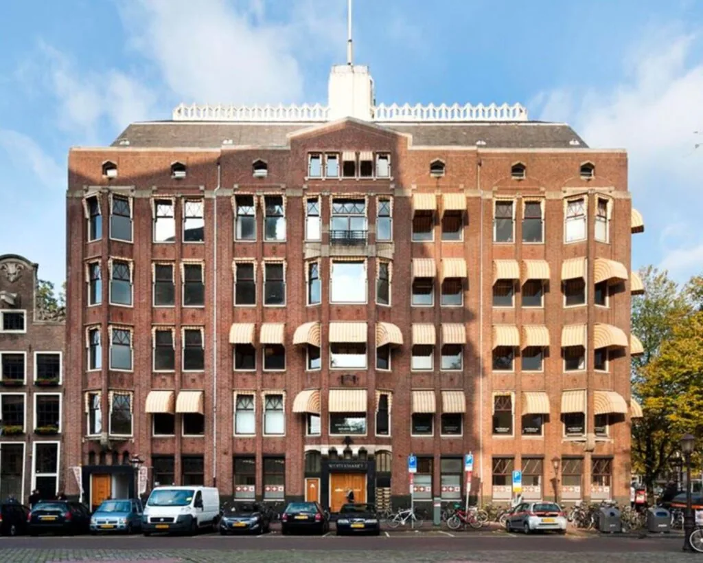 Vooraanzicht van een karakteristiek kantoorpand aan de Westermarkt 2 in Amsterdam met markante zonweringen en geparkeerde auto's ervoor.