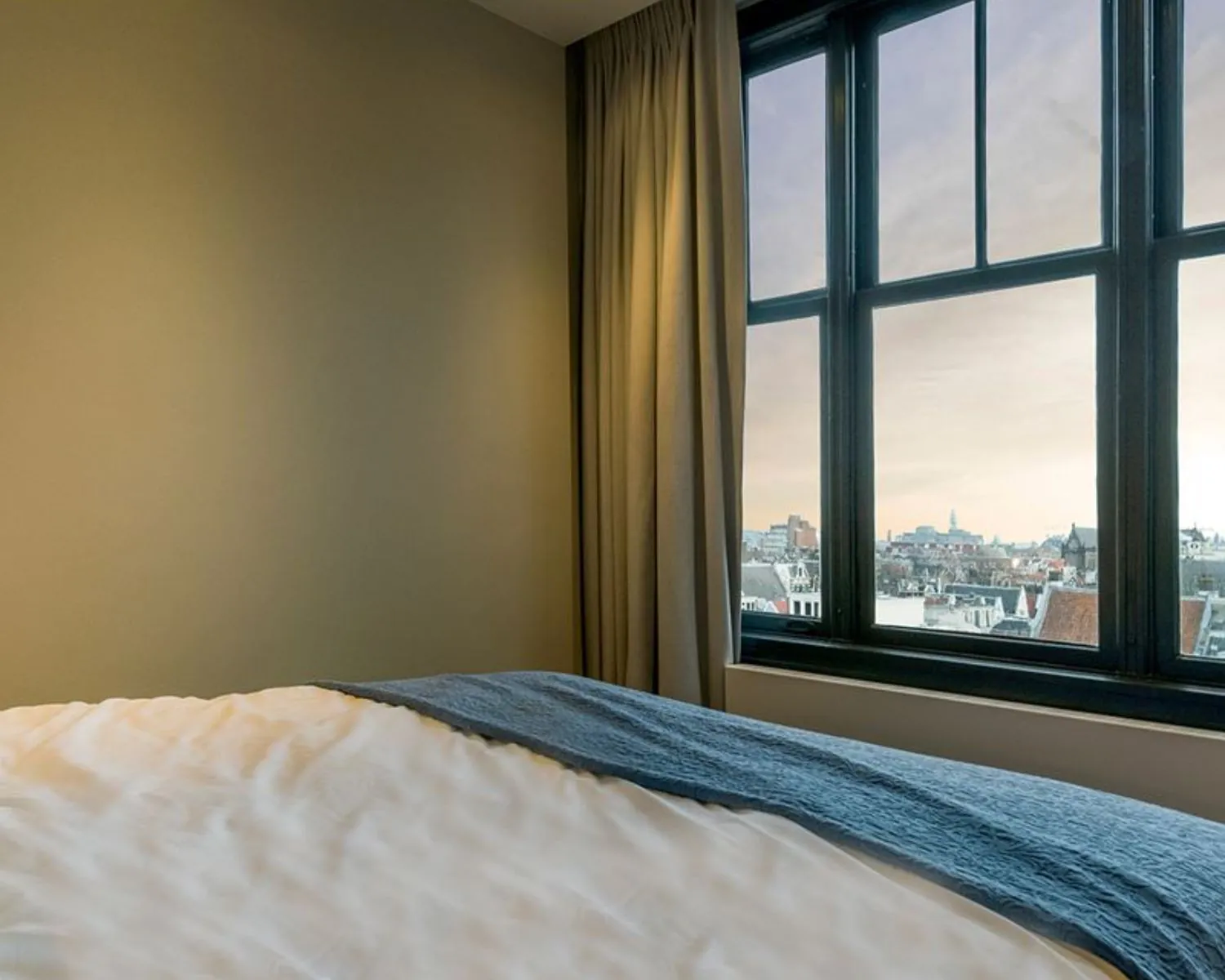 Slaapkamer met groot raam en uitzicht op de Amsterdamse binnenstad vanuit kantoorruimte aan de Westermarkt 2.
