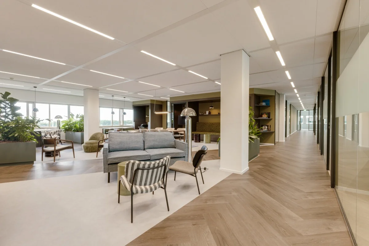 Een open, moderne kantoorruimte met zitgedeeltes, planten en veel natuurlijk licht.