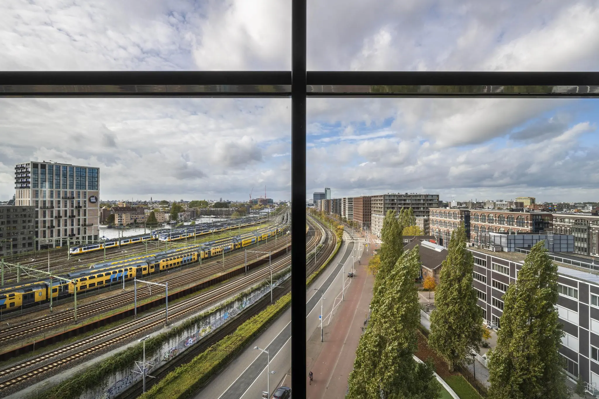 Uitzicht op Rietlandpark in Amsterdam met treinsporen, passerende treinen en omliggende moderne gebouwen.