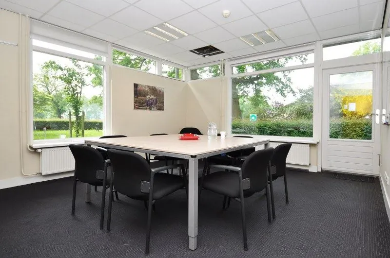 Vergaderruimte met zes stoelen rondom een tafel, grote ramen en uitzicht op groen aan de Spechtlaan.