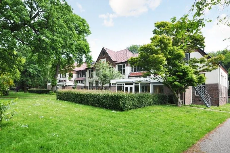 Groot gebouw aan de Spechtlaan omringd door een groen gazon en hoge bomen.