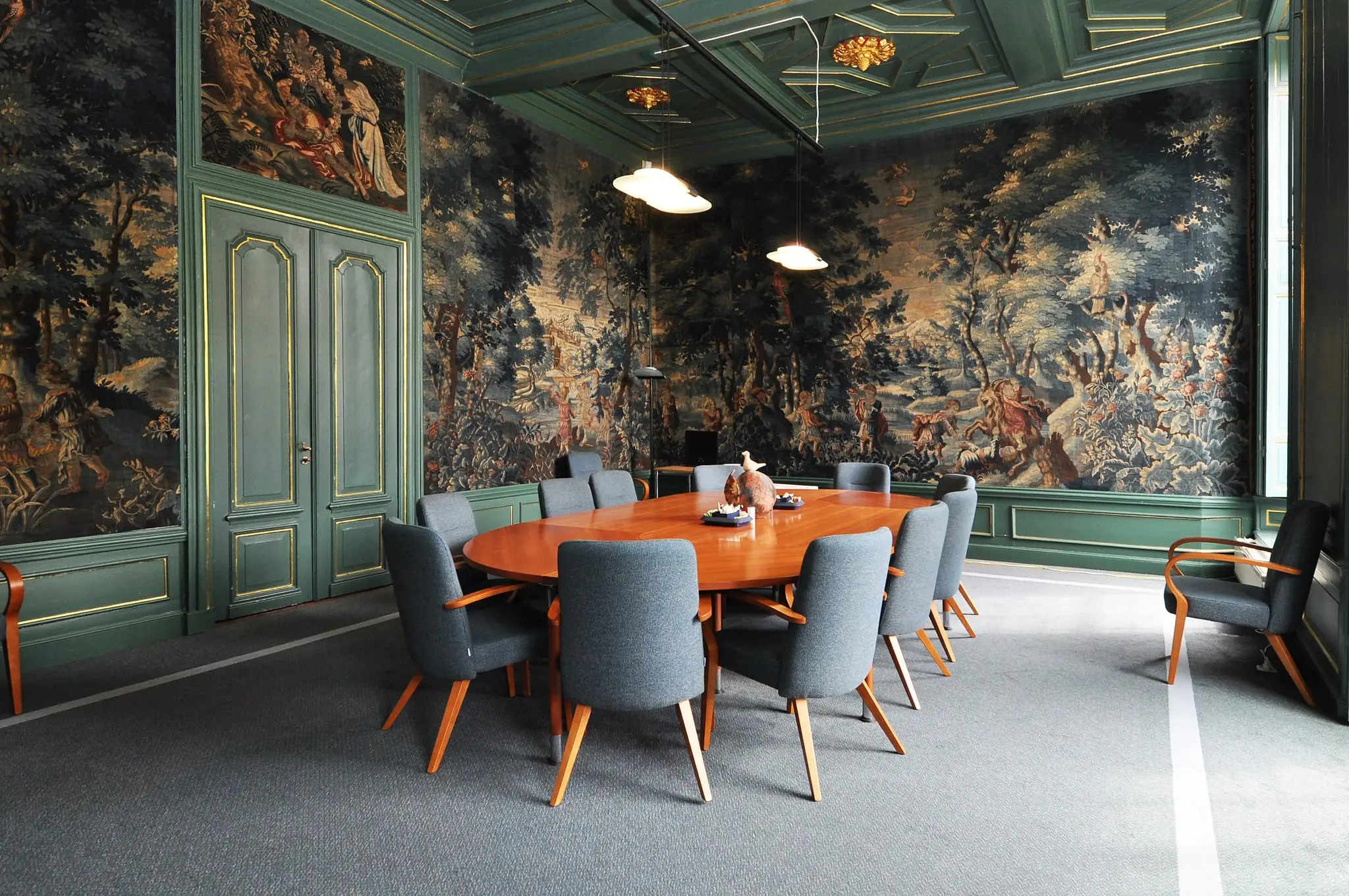 Vergaderruimte in Kasteellaan met houten tafel, stijlvolle stoelen en wandvullende wandtapijten met klassieke taferelen.