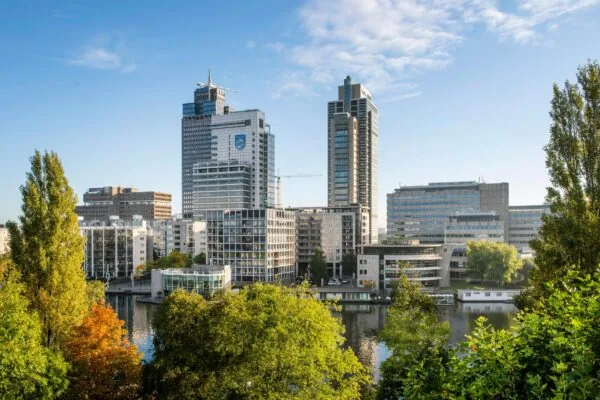 Zicht op de moderne kantoorgebouwen aan het Amstelplein in Amsterdam, met de Amstelrivier en groene bomen op de voorgrond.