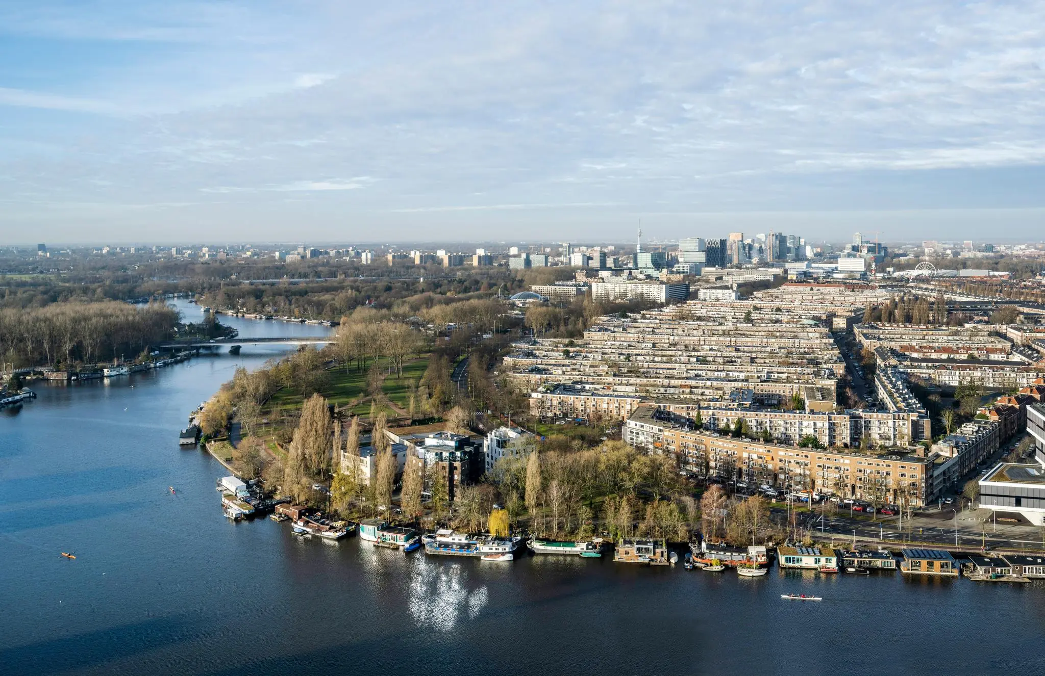 Luchtfoto van het Amstelplein in Amsterdam met woonboten langs de Amstel en de stad op de achtergrond.