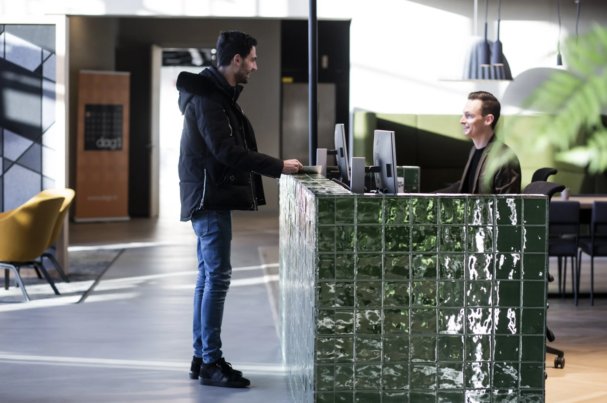 Man staat bij de receptiebalie van een modern kantoor aan de Atoomweg en wordt vriendelijk geholpen door een receptionist.