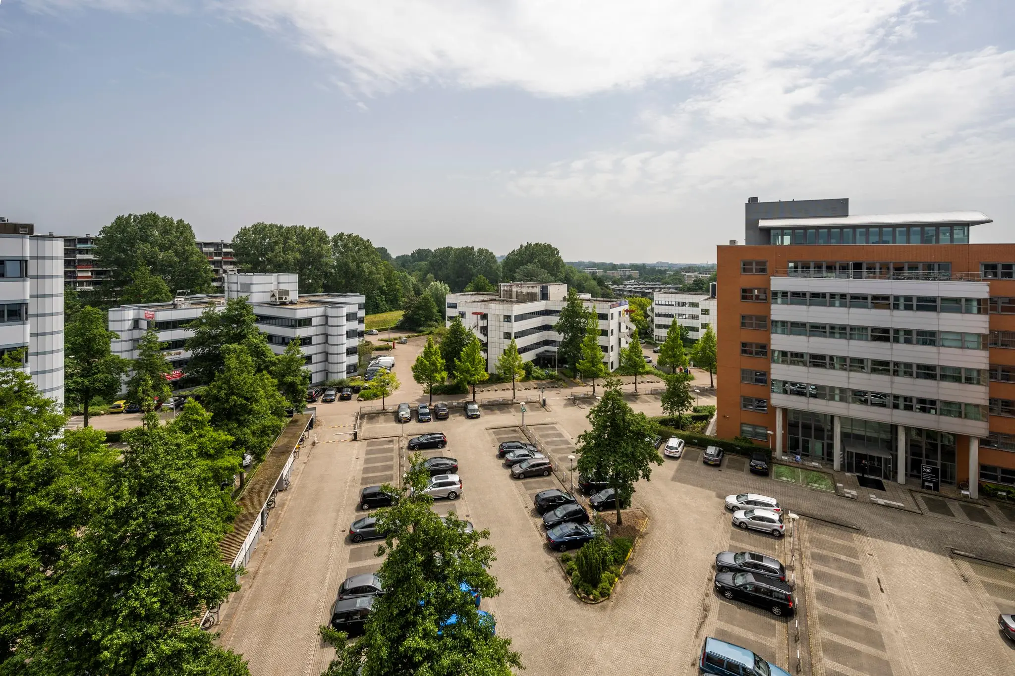 Luchtfoto van een kantoorgebouw met parkeerplaats en omliggende moderne kantoren in een groene omgeving.