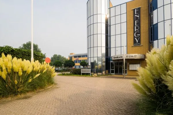 Ingang van het moderne kantoorgebouw Energy Building aan de Kernkade 8 t/m 12, omringd door siergrassen.