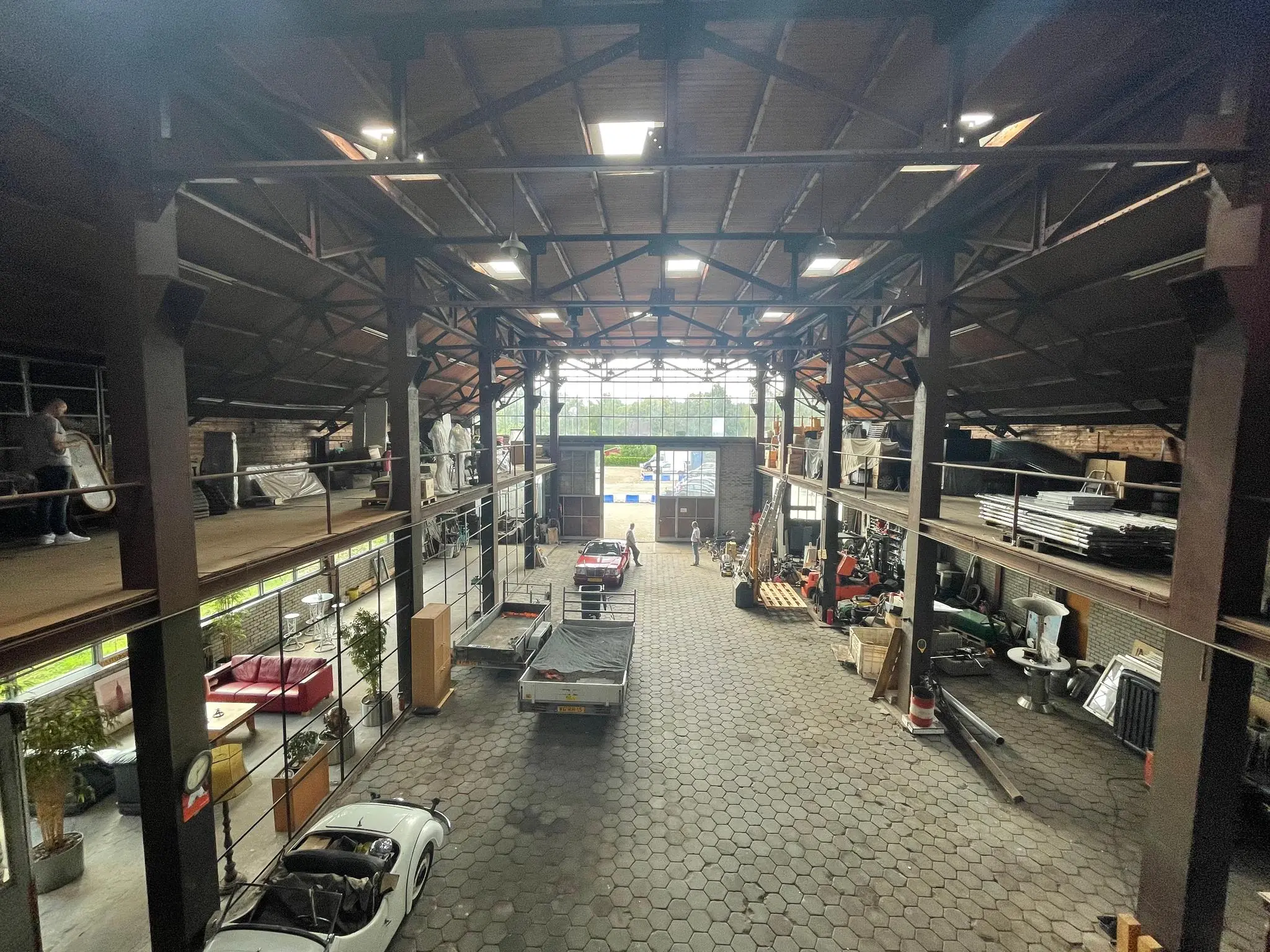 Interieur van een grote loods aan de Sloterweg met klassieke auto's, aanhangers en diverse opgeslagen materialen.