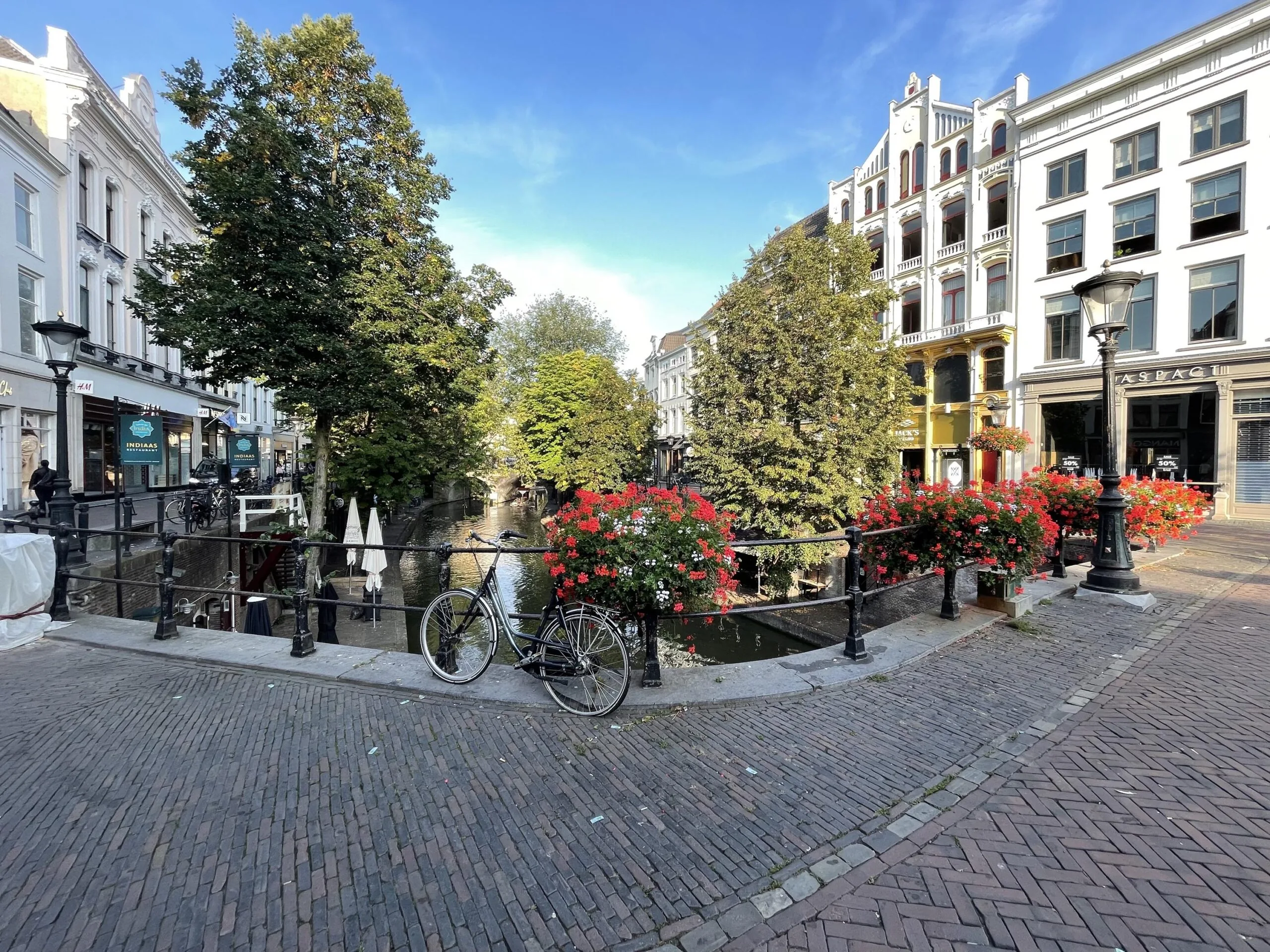 Stadstafereel van de Ganzenmarkt in Utrecht met fietsen, bloembakken en historische gebouwen langs de gracht.