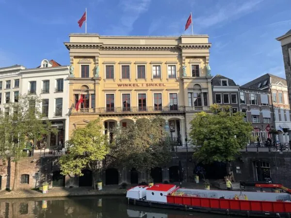 Een historisch gebouw met de naam "Winkel van Sinkel" aan een gracht, met een rode boot ervoor.