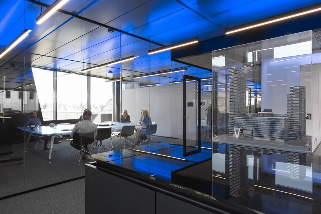 Vergaderruimte met glazen wanden, blauwe plafondverlichting en een maquette van gebouwen aan de Moermanskade.