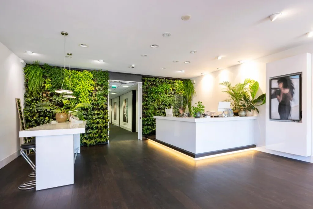 Moderne en frisse ontvangstruimte met groene plantenwand en witte balie bij Stammerhove.