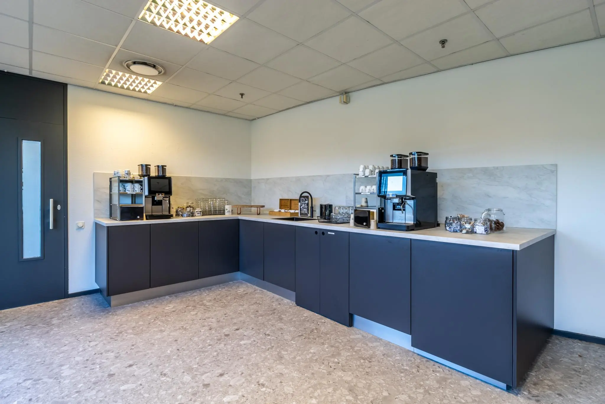 Moderne koffieruimte op Oudlaan met koffieautomaten, kopjes, glazen en snacks op een strak aanrecht.