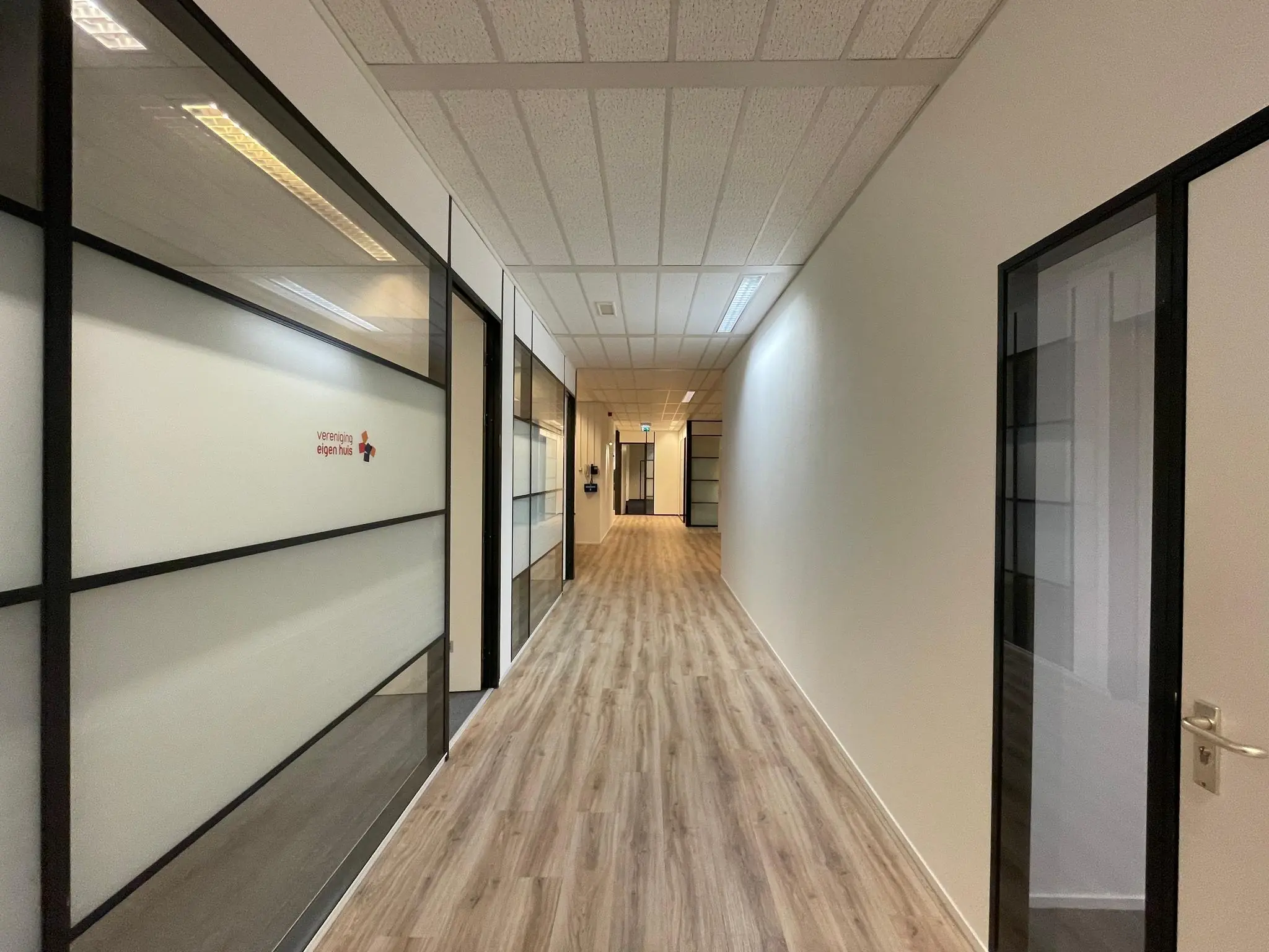 Lichte, moderne kantoorhal met glazen wanden en het logo van Vereniging Eigen Huis.