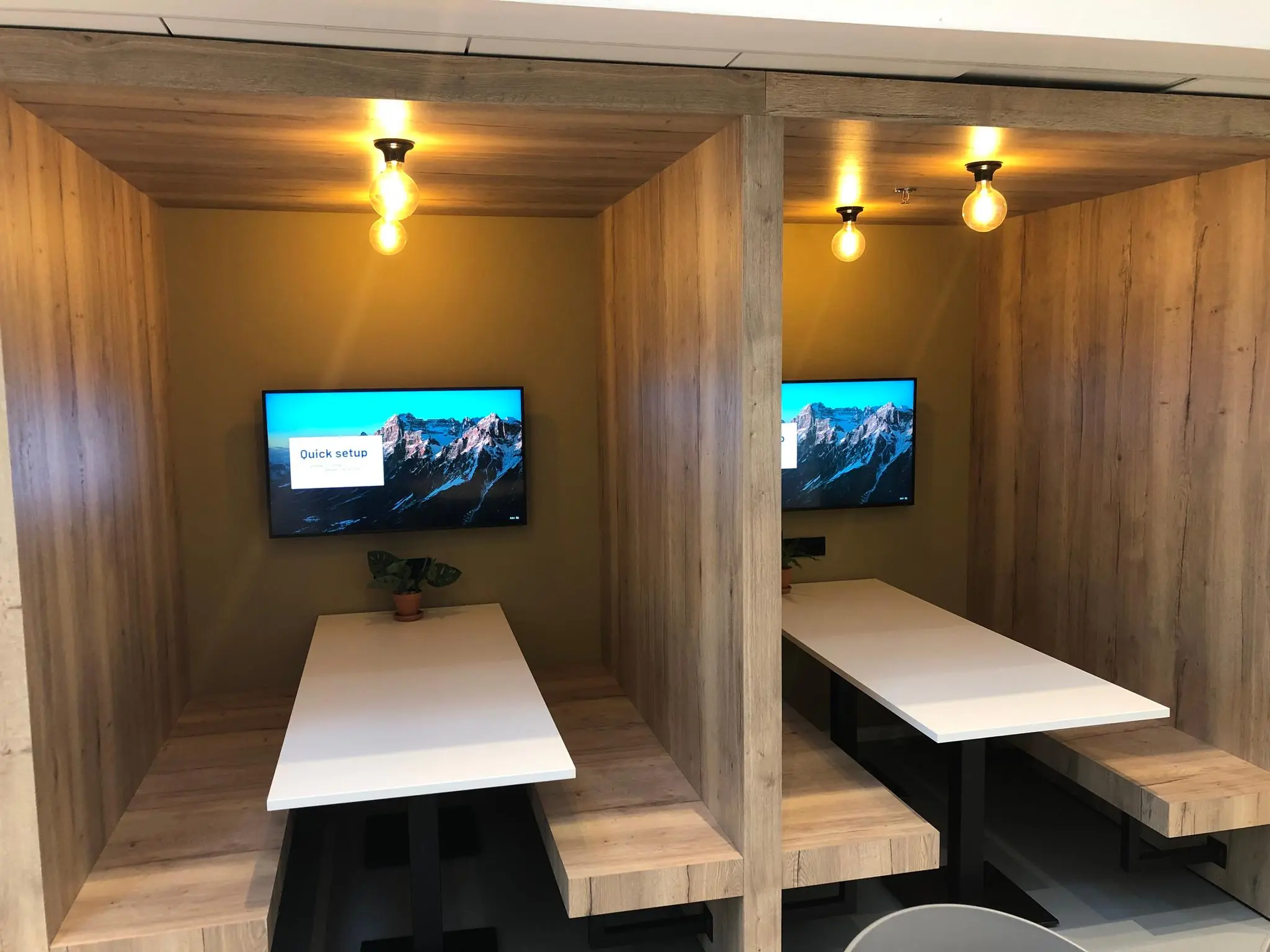 Twee moderne houten werkplekken met ingebouwde tafels, banken, tv-schermen en warme verlichting op Newtonlaan.