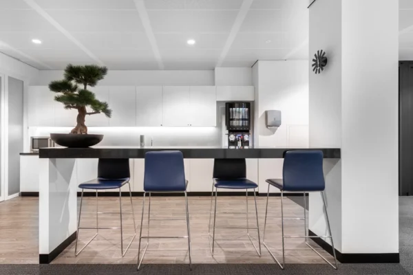 Een moderne keuken met een hoge tafel, vier blauwe stoelen en een bonsai-boom.