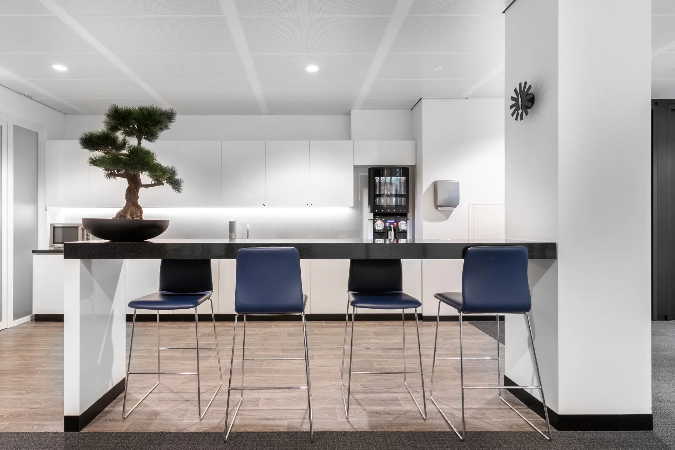 Een moderne keuken met een hoge tafel, vier blauwe stoelen en een bonsai-boom.