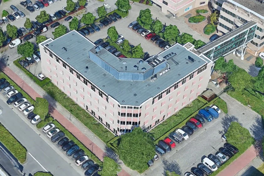 Luchtfoto van het kantoorgebouw 'De Wisselwerking' met omliggende parkeerplaatsen en groenstroken.