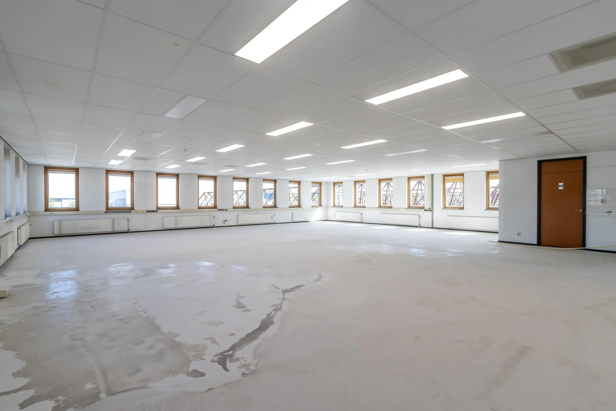 Leeg kantoorpand met systeemplafond, tl-verlichting en vele ramen aan beide zijden.