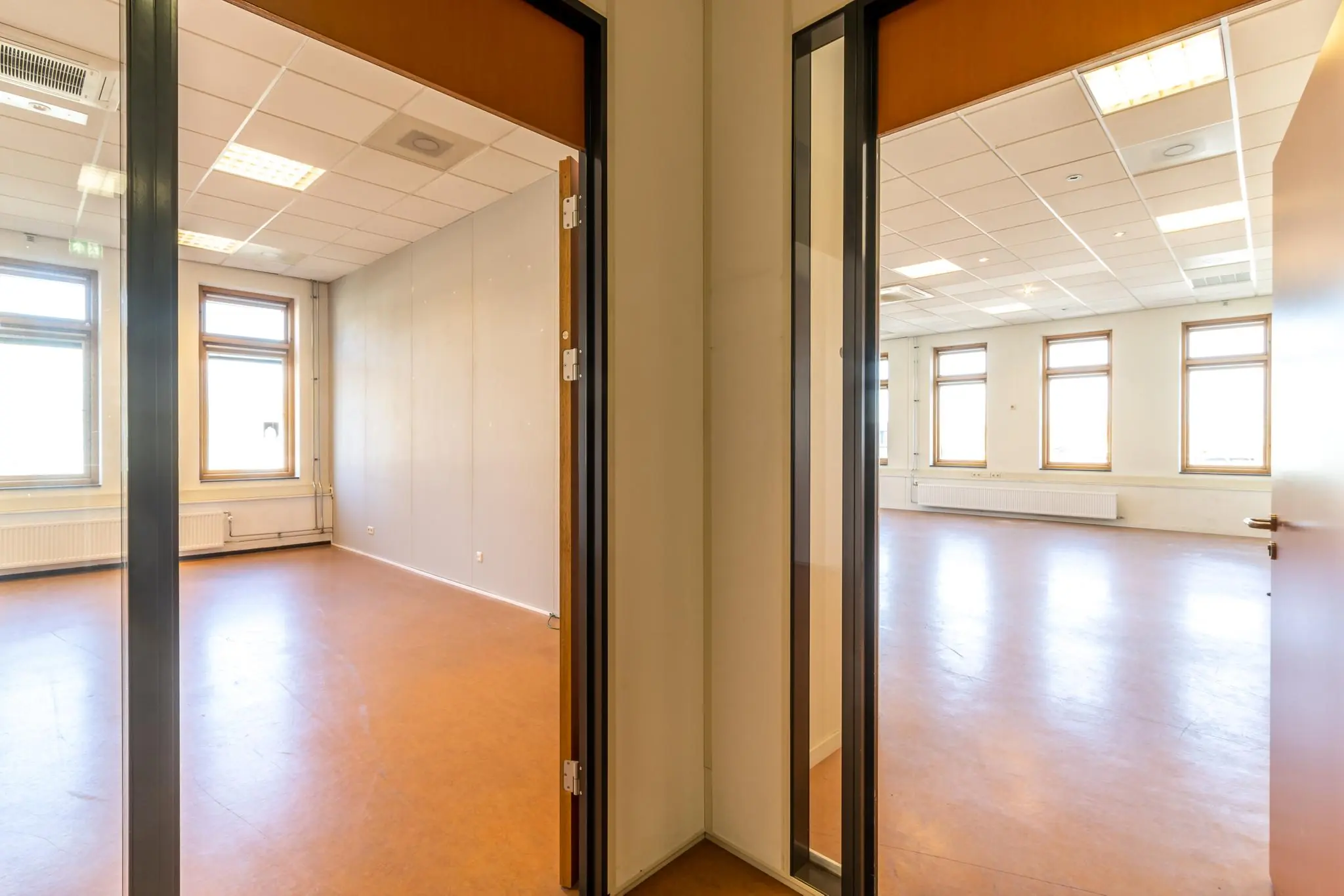 Twee aangrenzende, lichte kantoorruimtes in het gebouw Veldzigt met grote ramen en een systeemplafond.