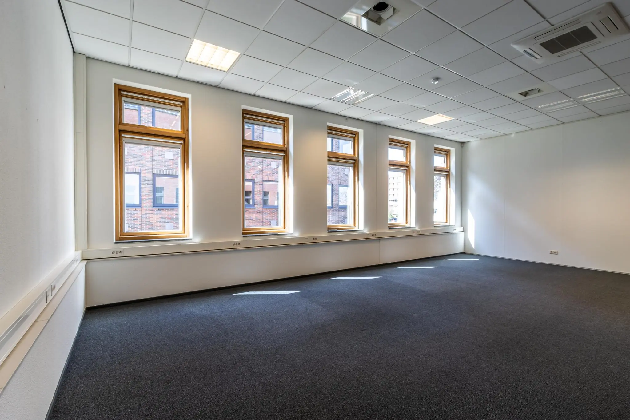 Lichte, lege kantoorruimte in gebouw Veldzigt met vijf hoge ramen en systeemplafond.