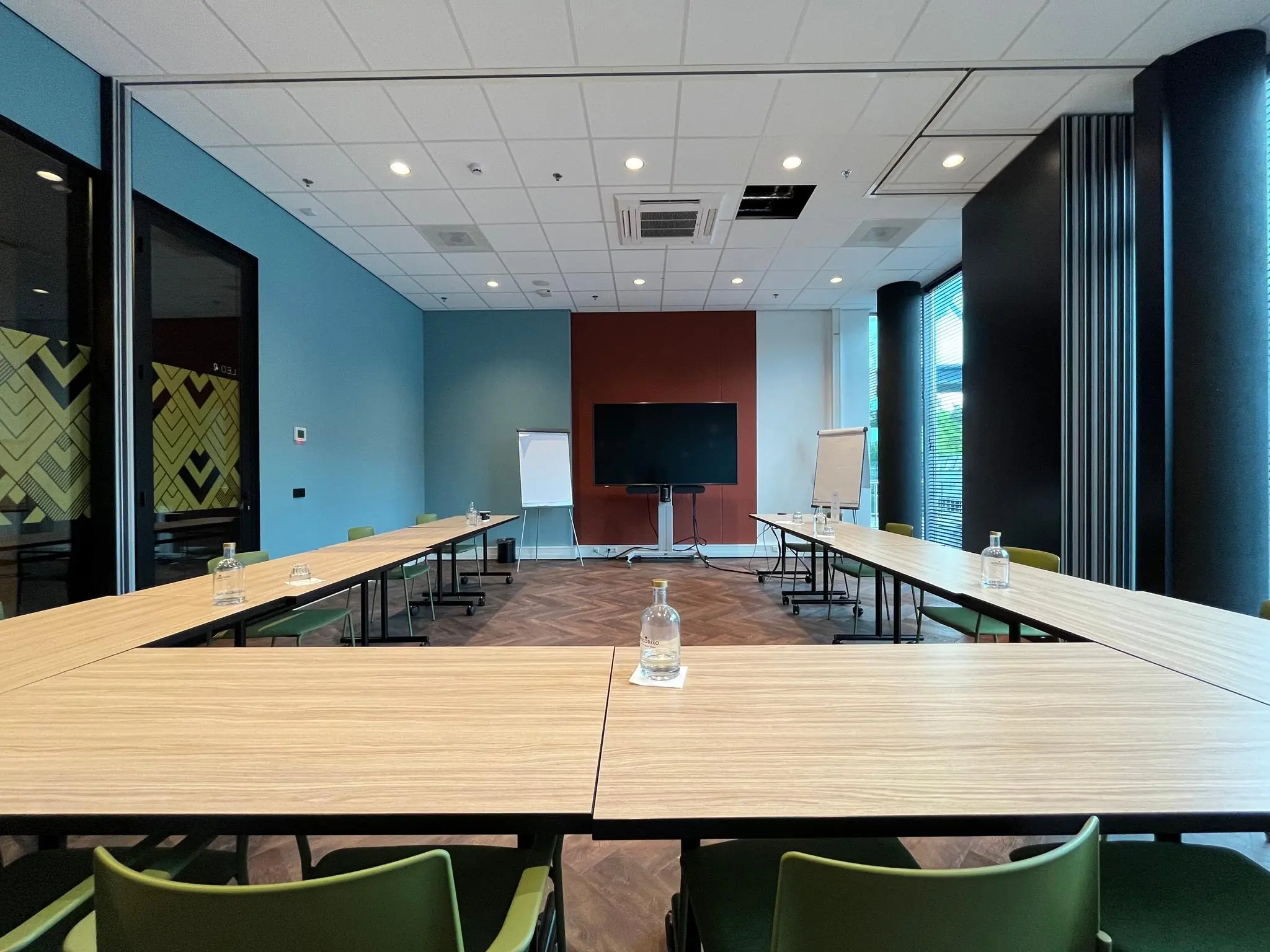 Vergaderruimte op het Herculesplein met U-opstelling, scherm, flip-overs en waterflessen op de tafels.