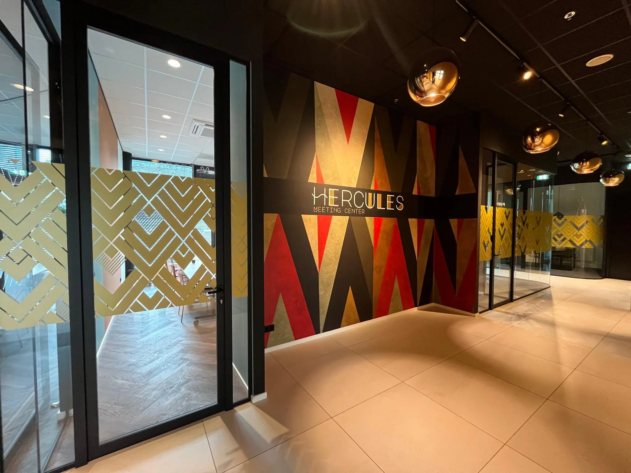 Ingang van het Hercules Meeting Center met kleurrijke wanddecoratie en glazen kantoorwanden.