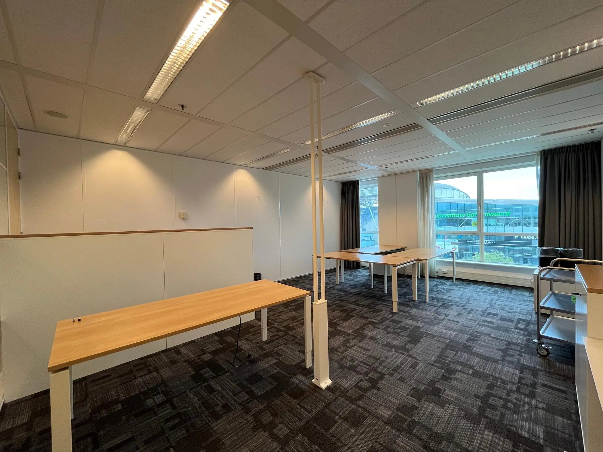 Kantoorruimte aan het Herculesplein met lege bureaus en uitzicht op het stadioncomplex aan de overkant van de straat.