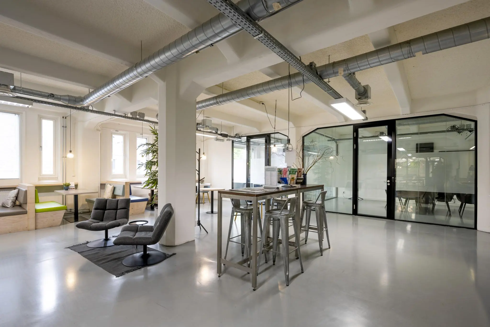 Modern ingericht kantoor met industriële uitstraling aan de Van Diemenstraat, met zitjes, hoge tafels en glazen vergaderruimte.