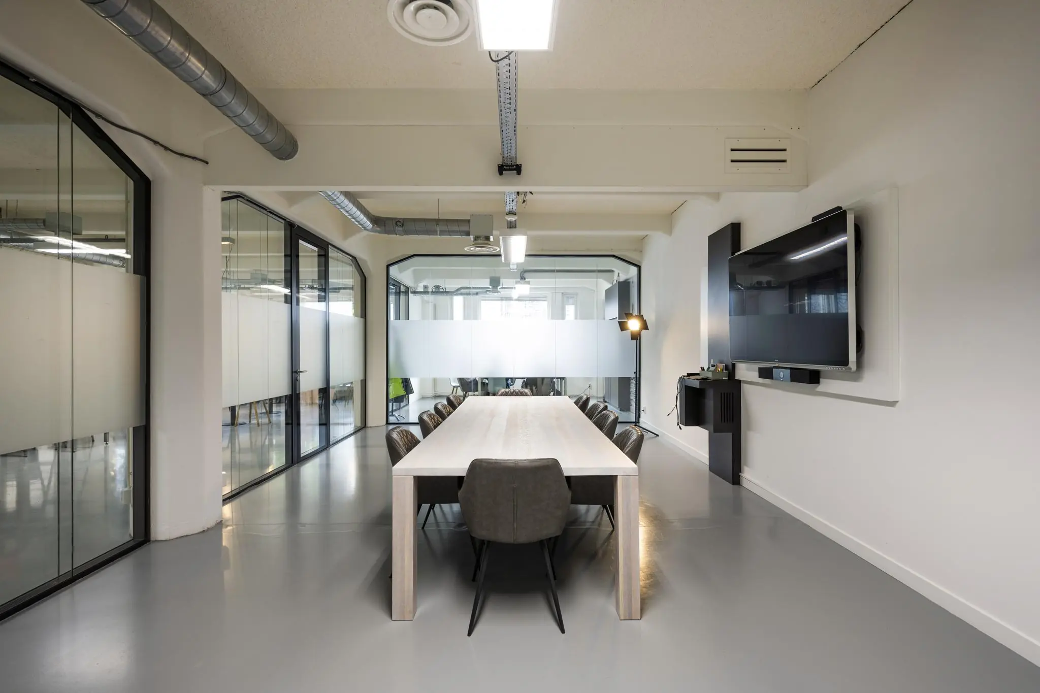 Moderne vergaderruimte aan de Van Diemenstraat met een lange tafel, leren stoelen en een groot digitaal presentatiescherm.