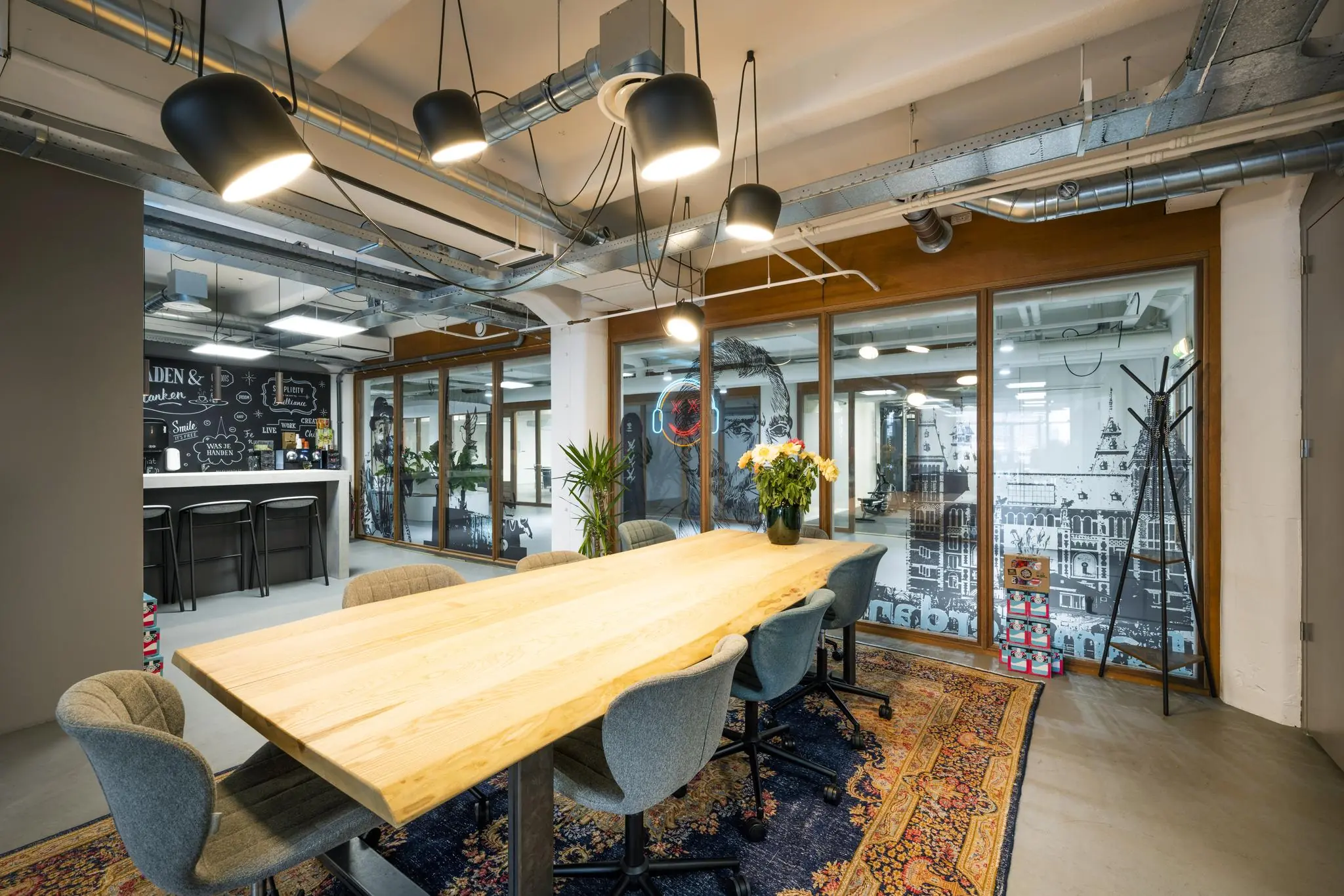 Moderne vergaderruimte aan de Van Diemenstraat met een houten tafel, designstoelen, hanglampen en glazen wanden met illustraties van Amsterdam.