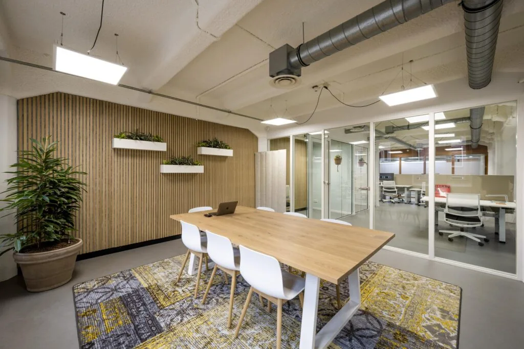 Moderne vergaderruimte aan de Van Diemenstraat met houten tafel, witte stoelen, planten en glazen wanden naar naastgelegen kantoor.