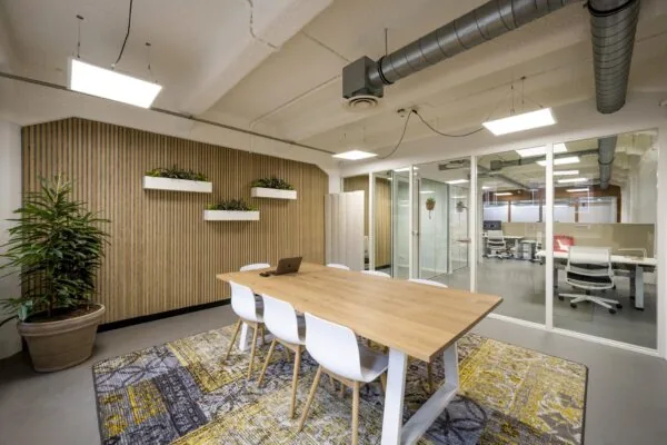 Moderne vergaderruimte aan de Van Diemenstraat met houten tafel, witte stoelen, planten en glazen wanden naar naastgelegen kantoor.