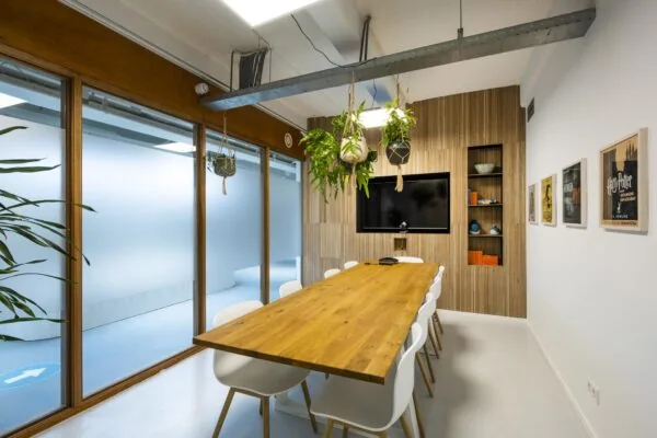 Vergaderruimte aan de Van Diemenstraat met houten tafel, hangplanten, ingebouwd scherm en moderne inrichting.