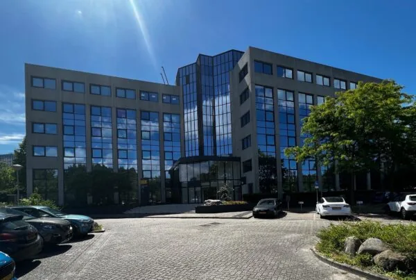 Kantoorgebouw Nevelgaarde met spiegelende ramen en geparkeerde auto's op een zonnige dag.