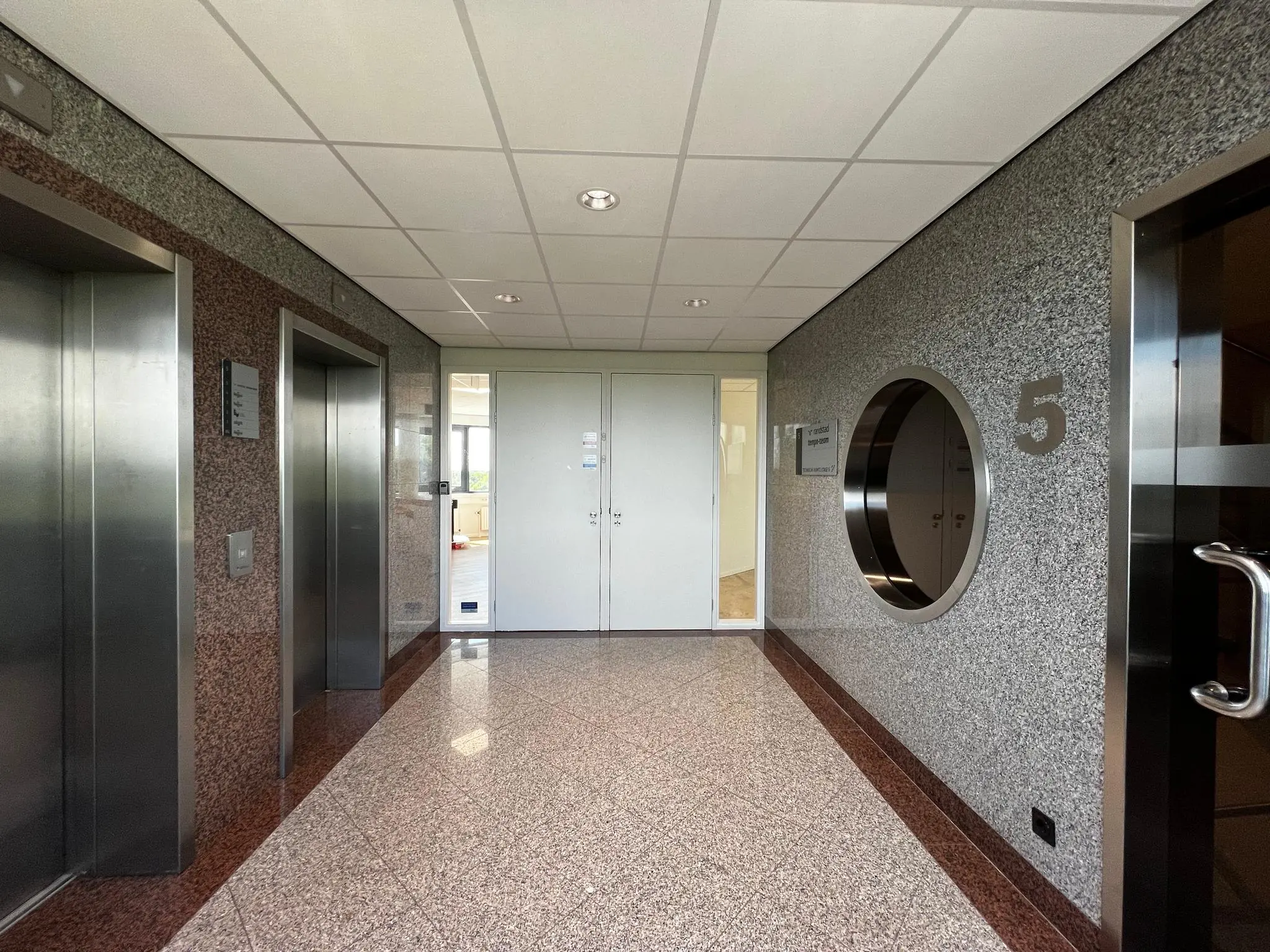 Hal met twee liften, een witte deur en het cijfer 5 op de muur in een kantoorgebouw aan de Nevelgaarde.