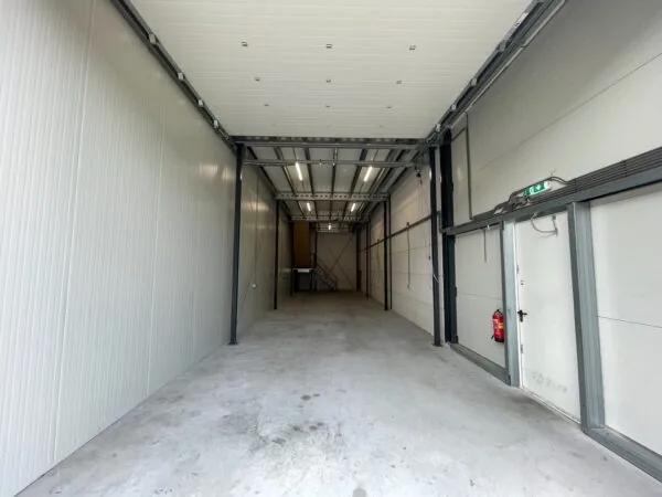 Lege, smalle bedrijfsruimte aan de Aalsmeerderweg met betonnen vloer en witte paneelwanden.