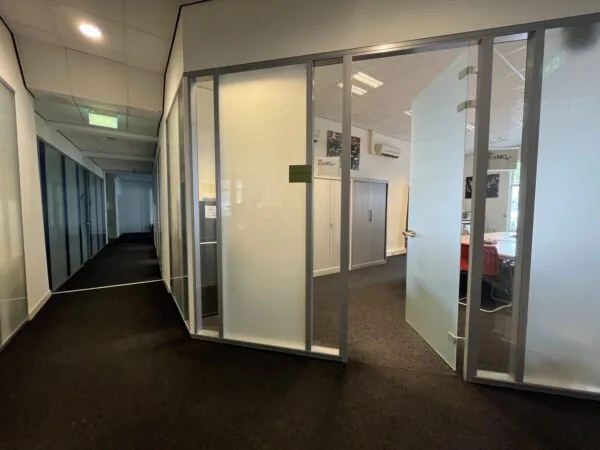 Een kantoorhal met glazen wanden en een open deur naar een vergaderruimte.