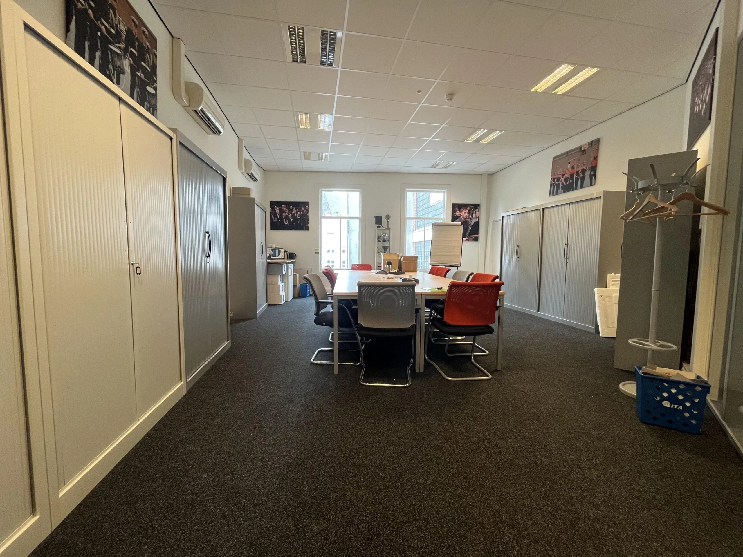 Een vergaderruimte met een lange tafel omringd door stoelen en kasten langs de muren.