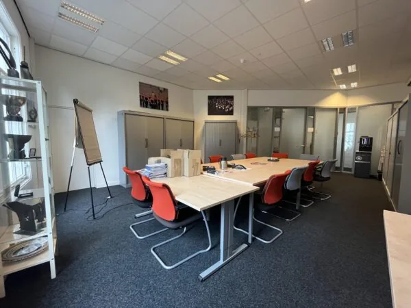 Een vergaderruimte met een lange tafel, rode en grijze stoelen, kastenaankleding en een flip-over.