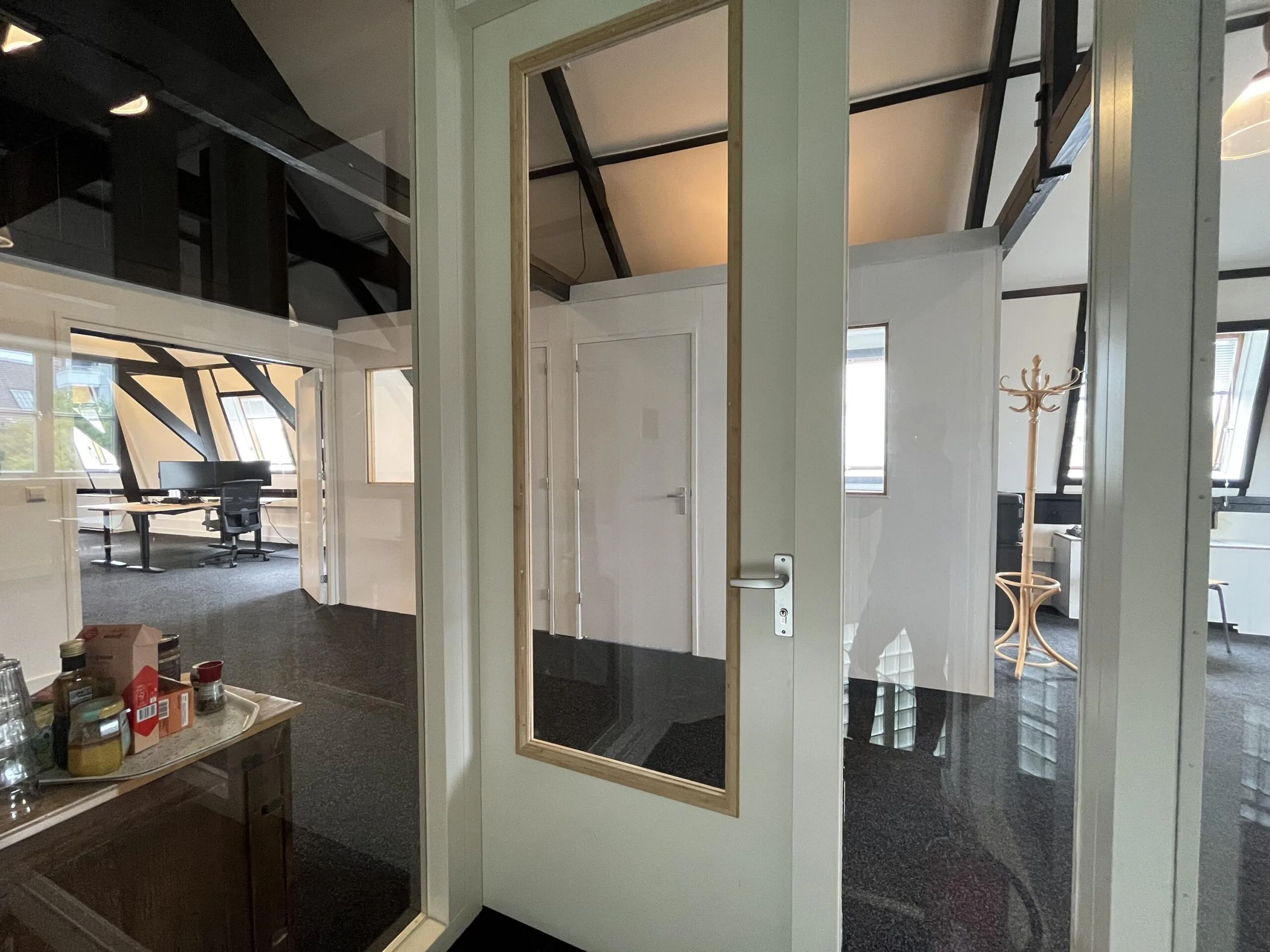 Een modern kantoorinterieur met glazen deuren en een ruimte met bureaus en een kapstok.