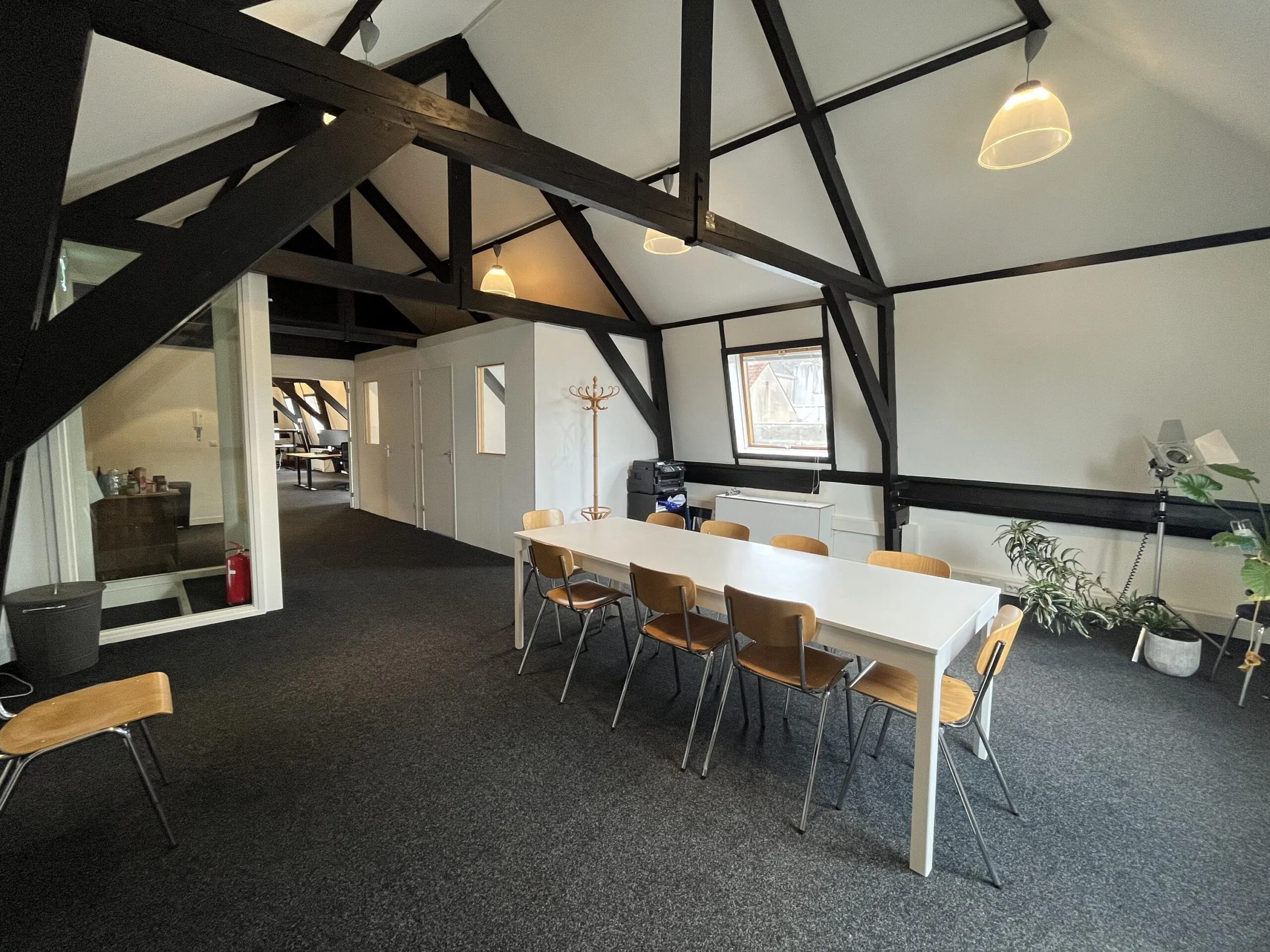 Een zolderkamer in moderne stijl met een lange witte tafel omringd door houten stoelen en een zichtbaar dakgebinte.