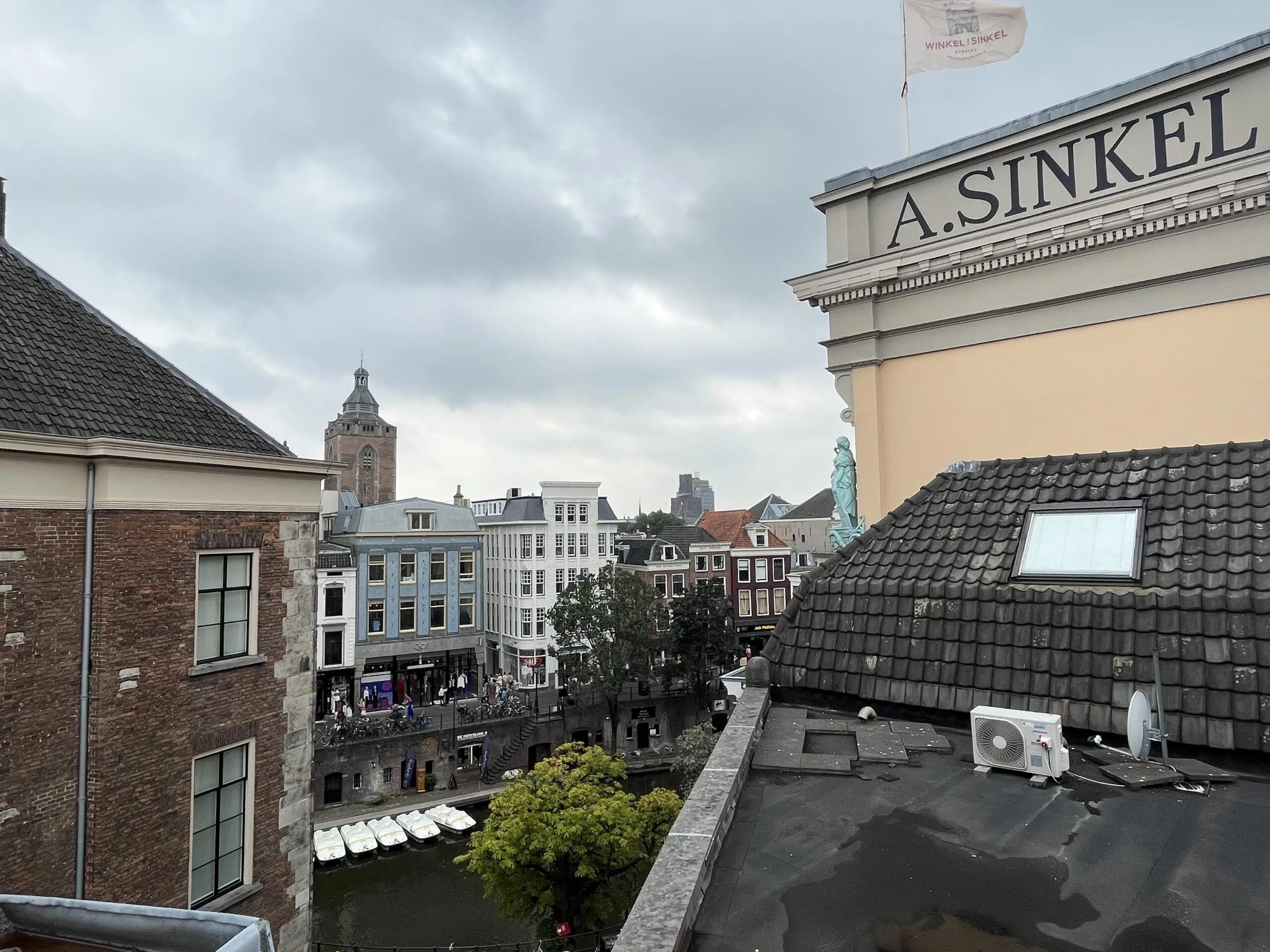 Uitzicht op de Ganzenmarkt met historische gebouwen en een kerk in de verte, gefotografeerd vanaf een dak met zicht op een gracht.