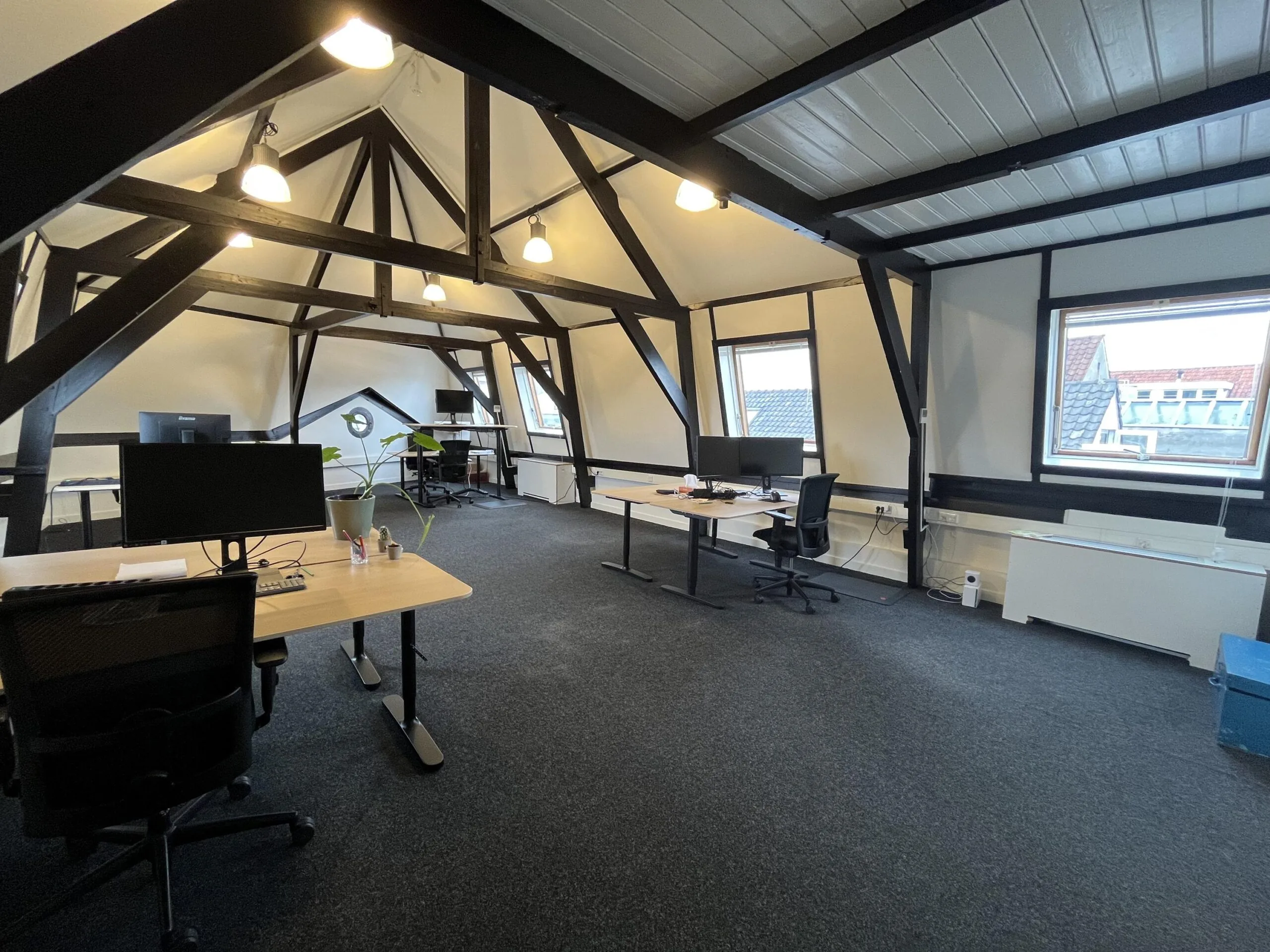 Een open kantoorruimte met houten balken en moderne bureaus op de Ganzenmarkt.