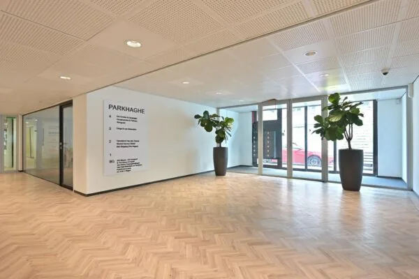 Moderne entreehal van kantoorgebouw ParkHaghe met houten visgraatvloer, glazen deuren en grote plantenbakken.